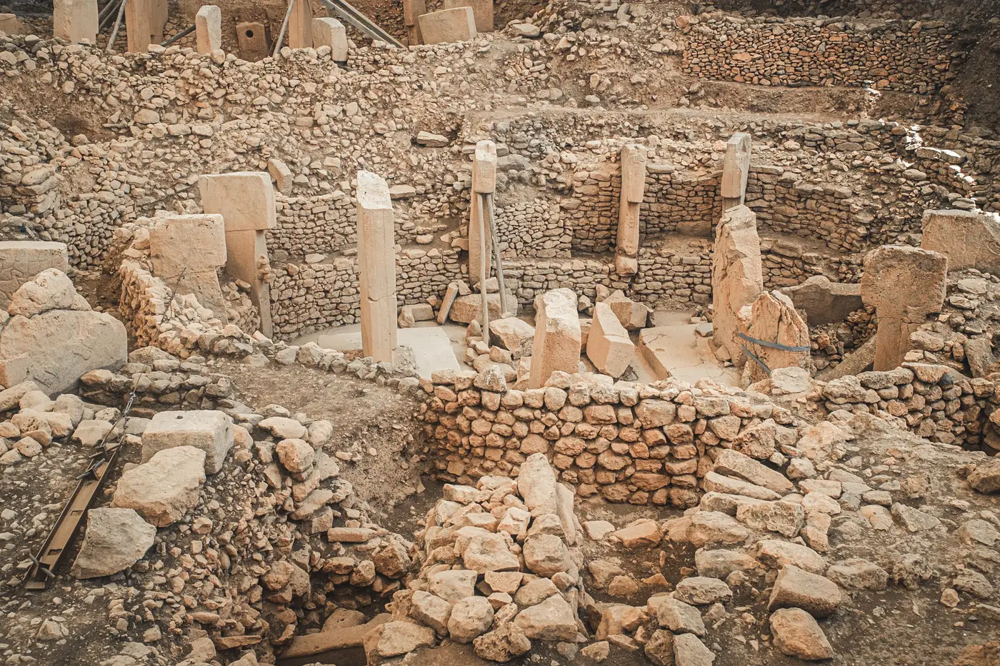 Aerial view into an excavated archaeological pit showing stone-walled compartments and standing stone pillars.