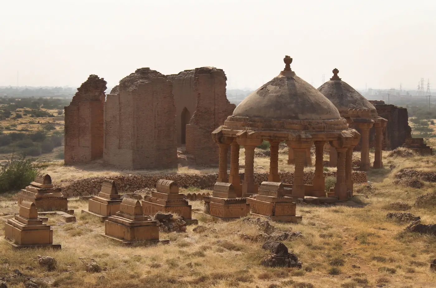 A remote necropolis of domed stone tombs and burial markers scattered across a dry, open plain.